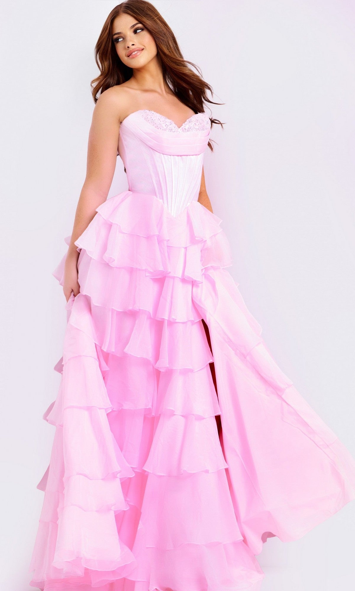 A woman in the Jovani 47762 long prom dress with a strapless satin corset bodice and ruffle-tiered chiffon skirt stands against a white background, holding part of her skirt to the side.